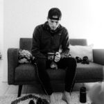 Barefoot man on couch with coffee mug and running gear at his feet