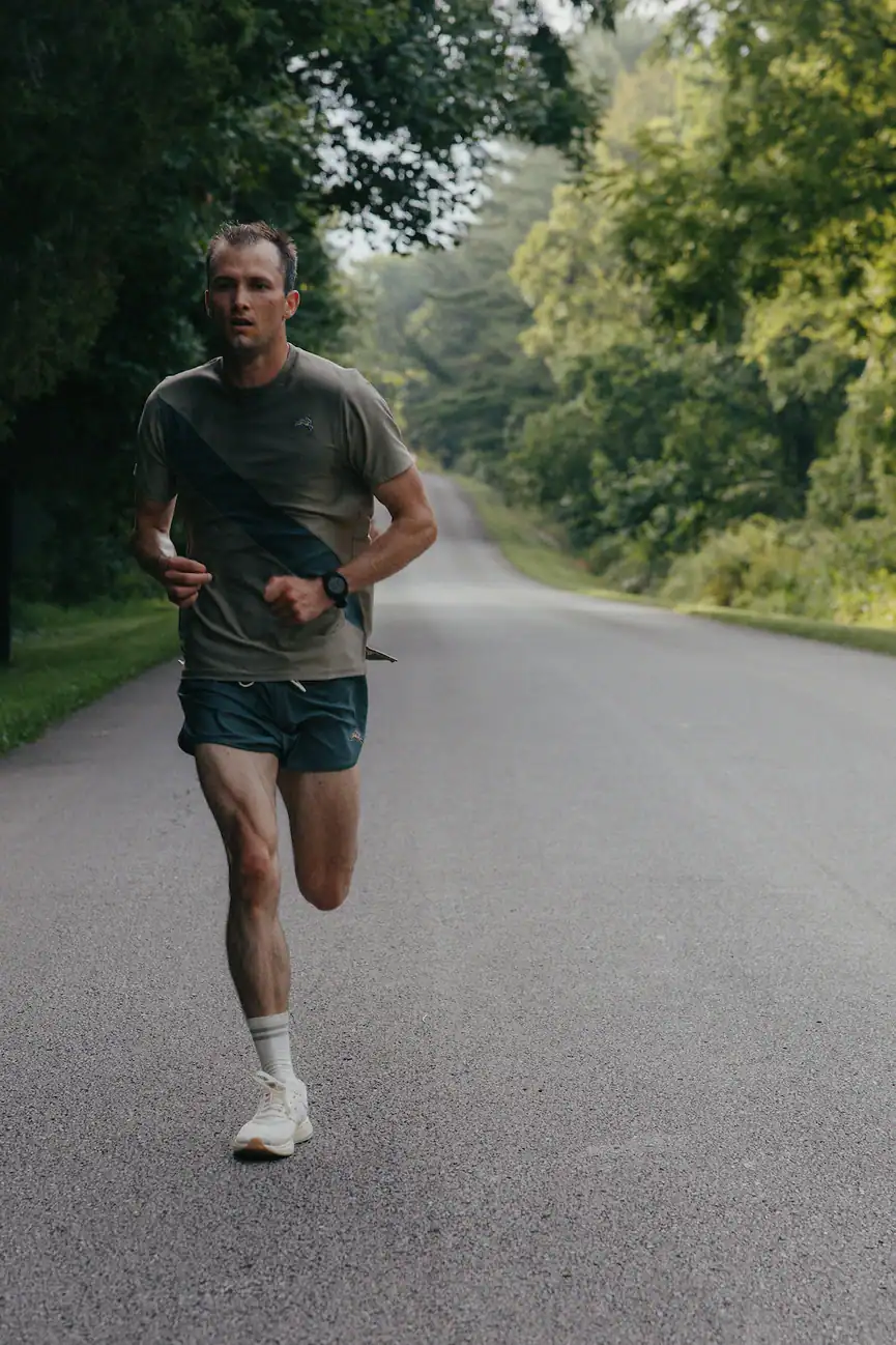 Solo runner in running gear training on an empty paved road surrounded by greenery