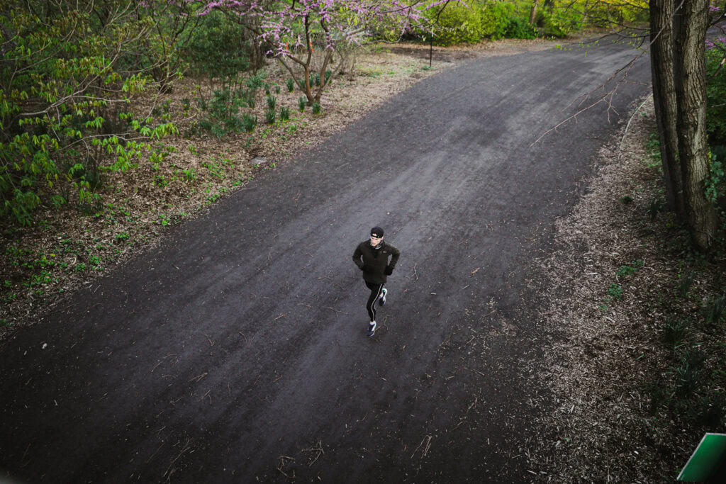 Runner in black gear on a wide dirt trail surrounded by budding trees in Central Park