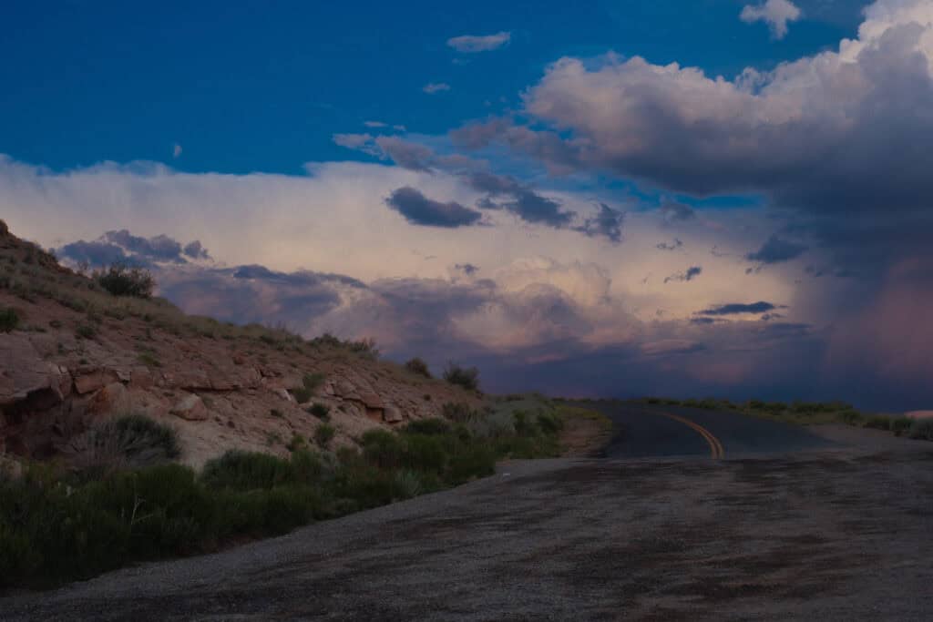 A winding road curves through a rocky desert landscape beneath dramatic evening clouds