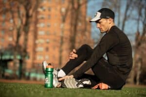 Runner stretching hamstring on turf beside Gatorade bottle