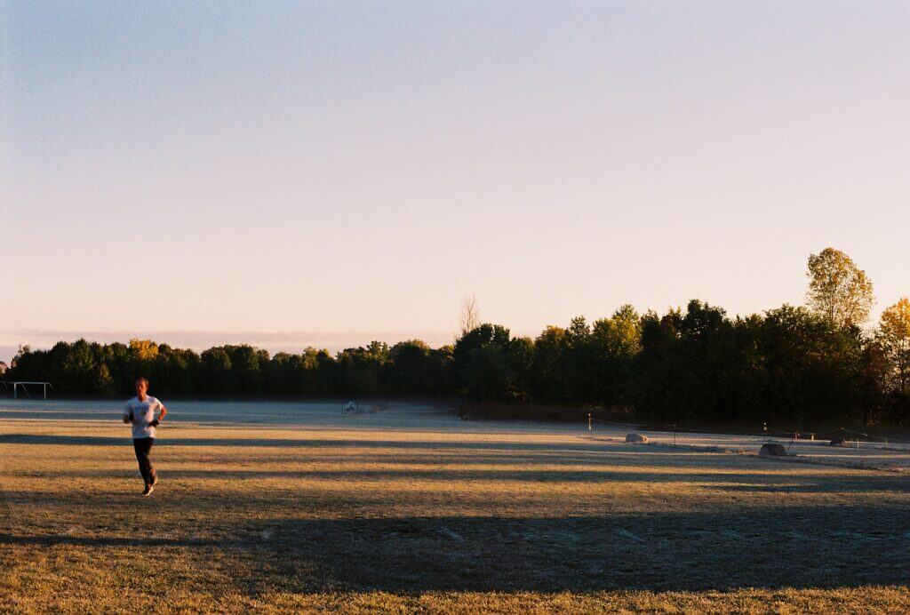 Single runner jogging across a frosty grass field at sunrise with trees in the background