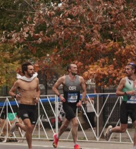Three male runners chatting mid-race during the NYC Marathon with fall leaves in the background