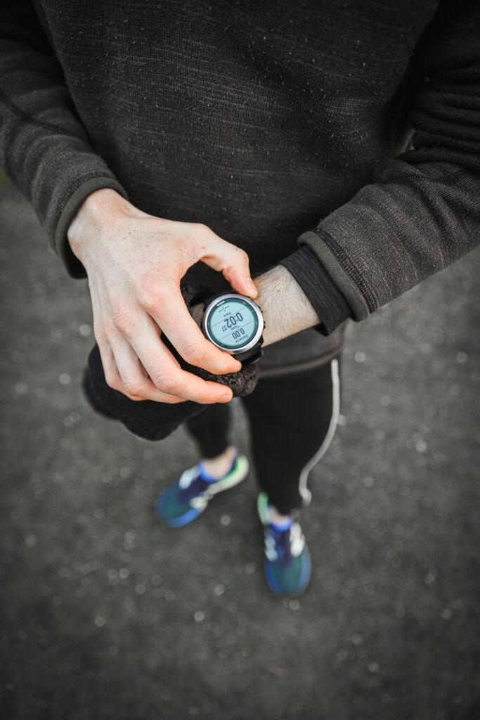 Runner checking GPS watch before a workout on asphalt path
