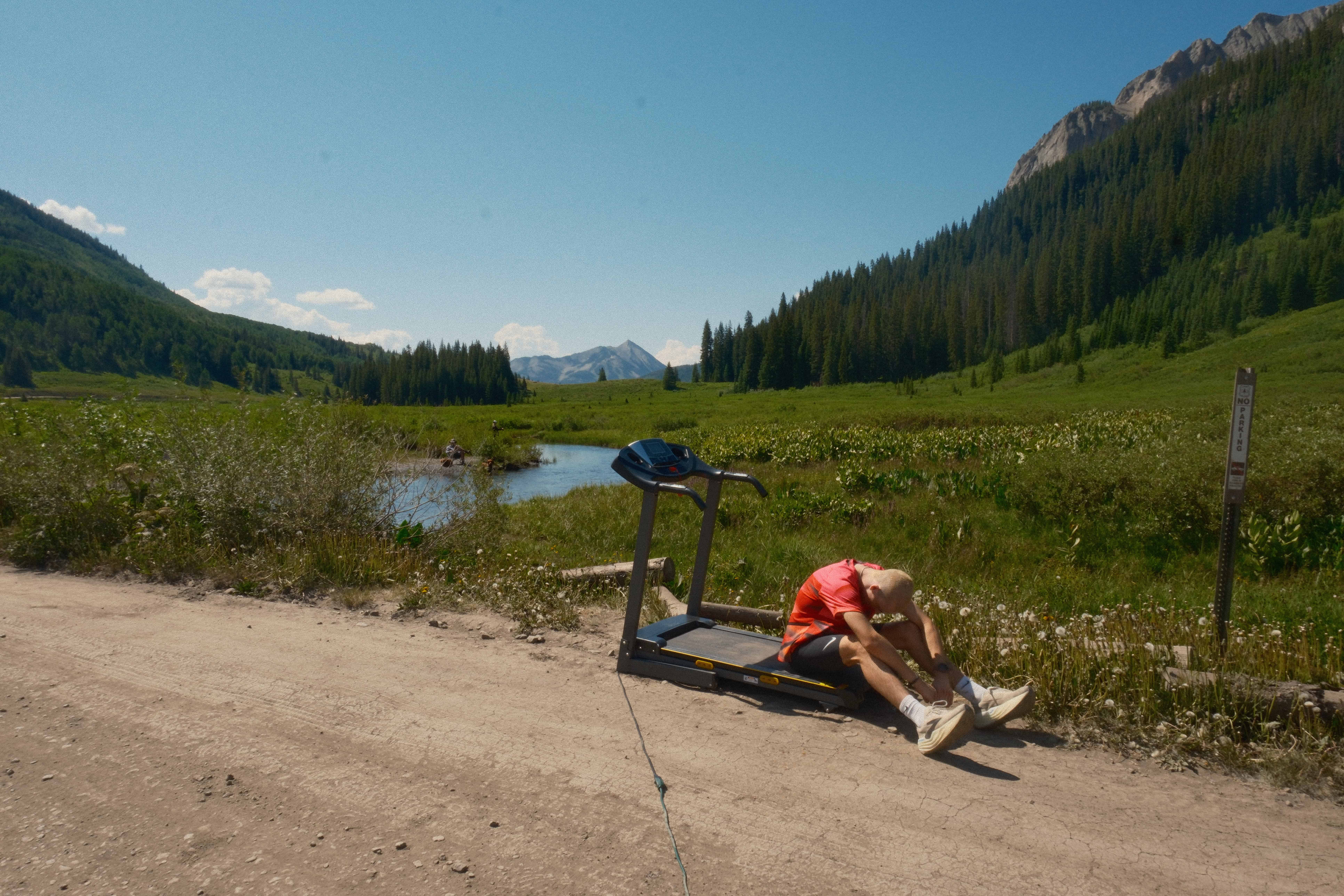A male runner sits slumped beside a treadmill in a mountain landscape after a hard workout